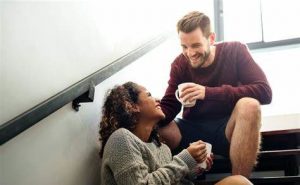 happy couple sharing a cup of coffee sitting on stair